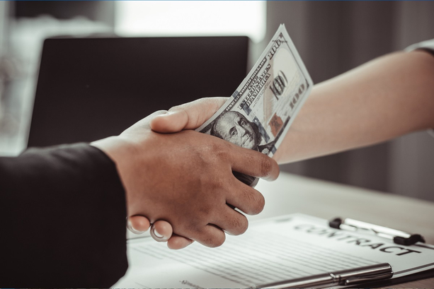 Two people shaking hands while holding money