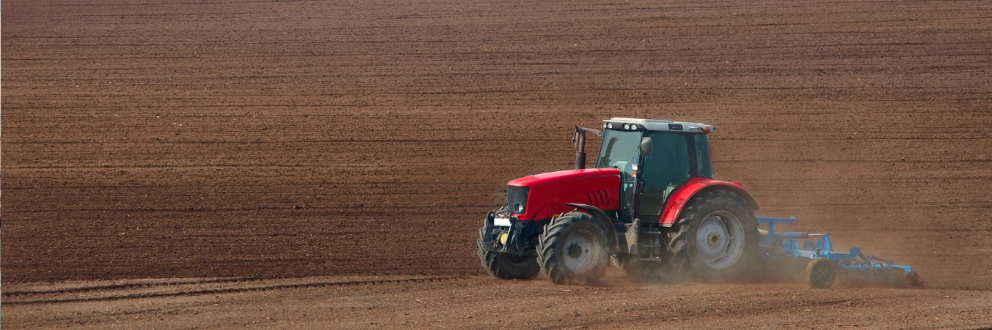 A red tractor cultivating a field.