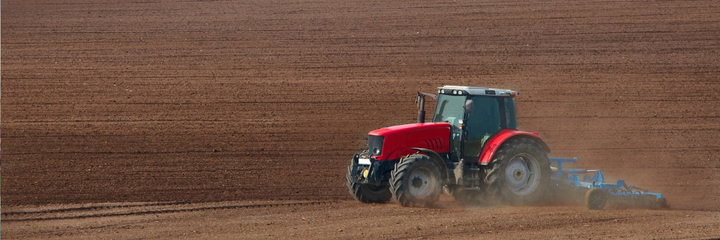 A red tractor cultivating a field.