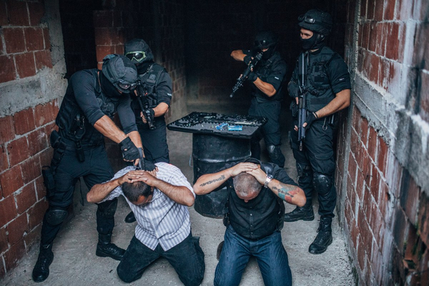 Tow men being arrested by armed police inside a bare brick building